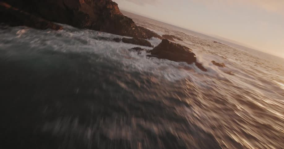 Aerial view of a rocky crust surrounded by the sea at dawn with sun reflection