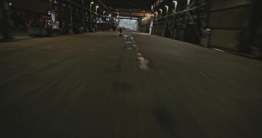A person rides a moped down a wet industrial looking corridor with overhead lighting