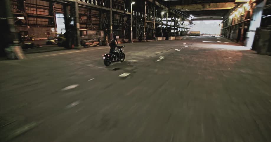 Aerial view of a person riding a motorcycle inside a long warehouse
