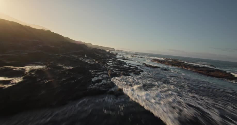 Aerial view of ocean waters reaching coastal rocks at dawn