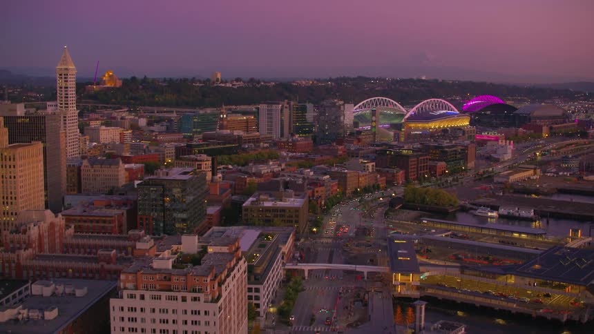Seattle at dusk with vibrant hues of purple and orange lighting up the skyline and reflecting off the citys iconic stadiums and skyscrapers