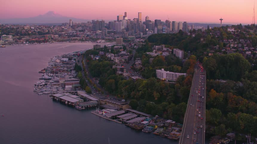 Seattle stretches out under a pinkish sky at dusk with the space needle rising above the landscape and mount rainier in the background framing the scene