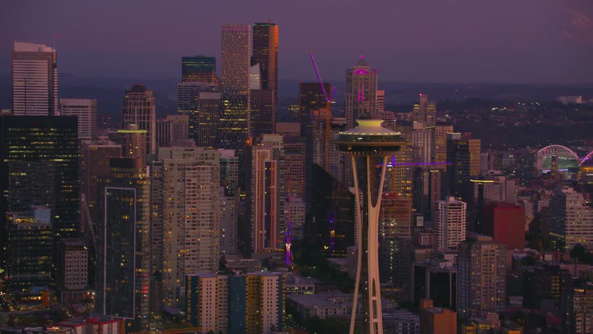 Space needle stands illuminated in the heart of seattle surrounded by glittering skyscrapers under a purple dusk sky
