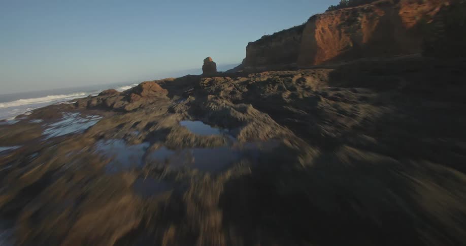 Aerial view of the sea crashing into a rocky and wooded coastline