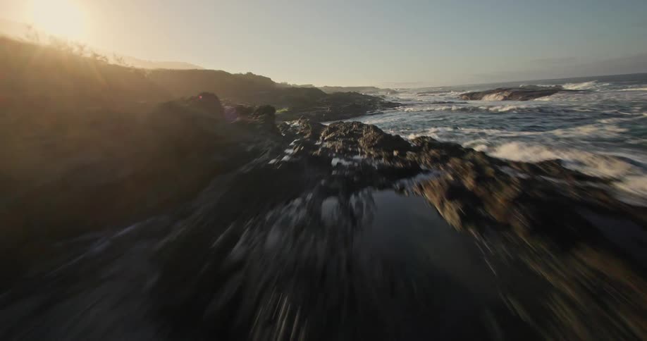Aerial view of a rocky crust by the sea with the sunrise on the horizon
