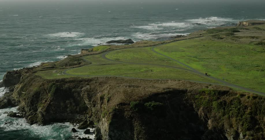 Aerial panorama of a green field on the rocky coast by the sea