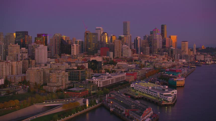The seattle skyline glows in the purple twilight reflecting its golden lights on the calm waters of puget sound