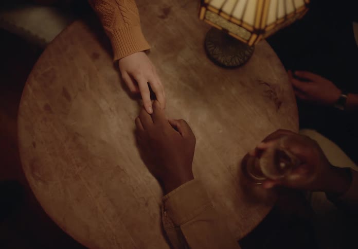 Couple holding hands at a bar table with drinks and other people around