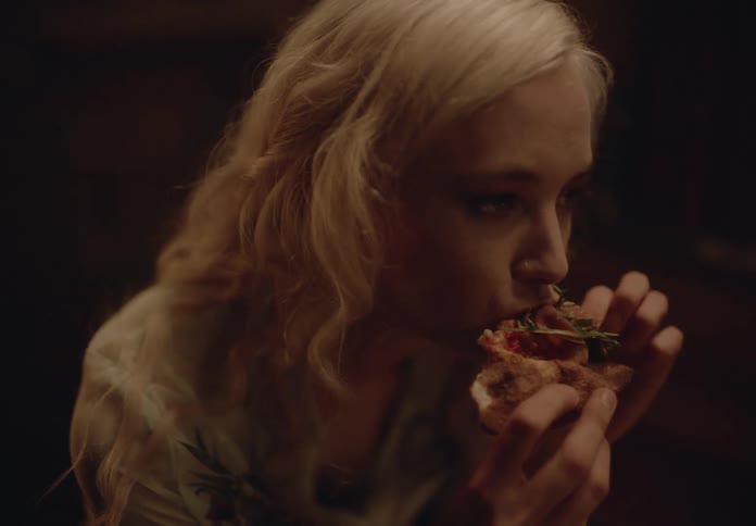 Blonde woman eating a slice of pizza and talking