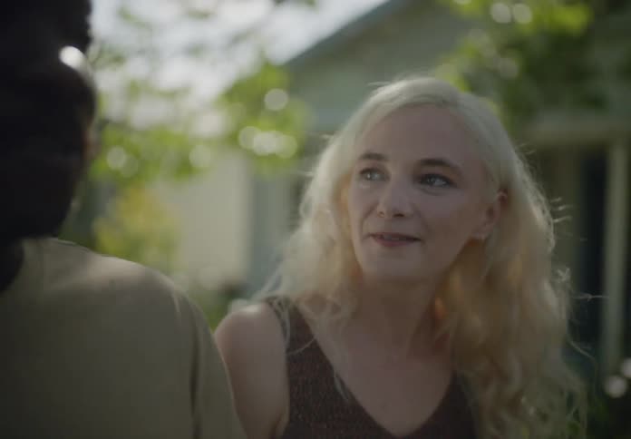 A woman with long blonde hair is walking outdoors in a residential area talking with a friend
