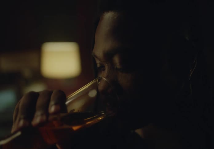 Close up of a man drinking beer from a tall grass on a dimly lit bar