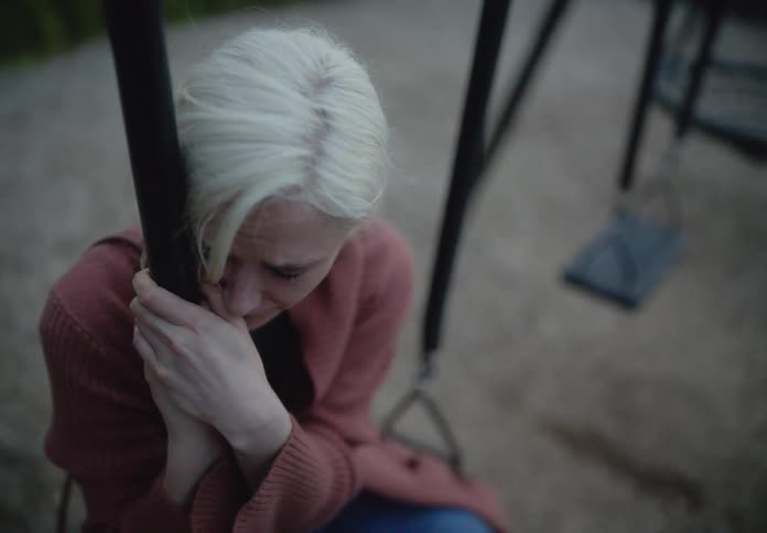 Woman in a park sitting on a swing sad