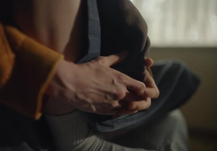 Closeup of the hands of a woman sitting on a bed squeezing and twisting a blanket