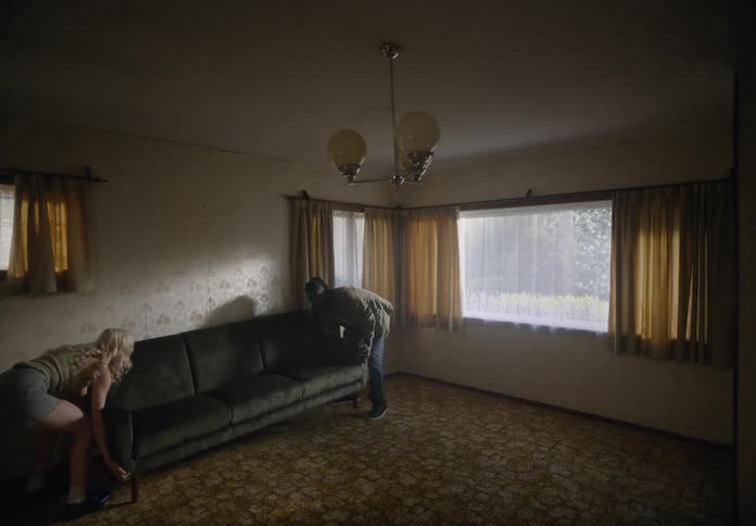 Woman and a man placing a sofa in the living room and both sit together