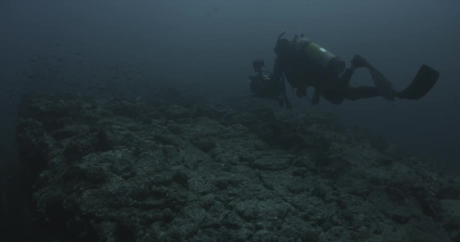 A scuba diver with a camera swims along the ocean floor