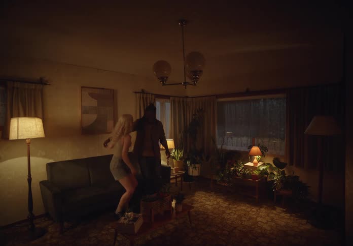 A young couple sits comfortably cuddling on the couch in a dimly lit living room