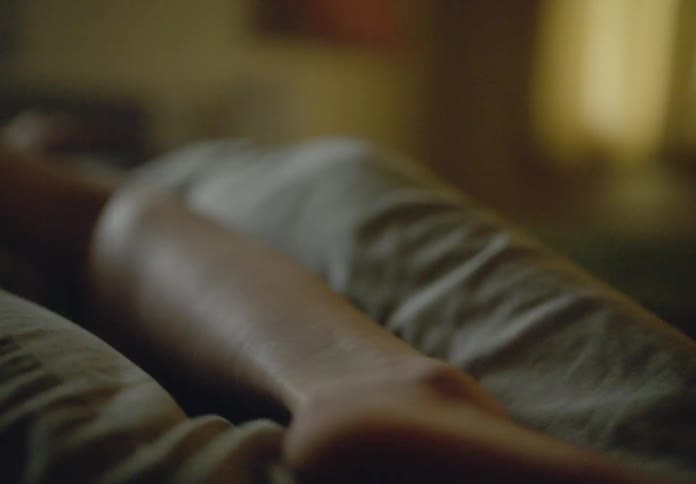 A womans arm and part of her torso rest on a blanket on the bed in the bedroom