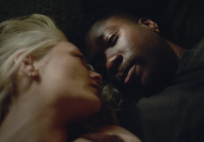 A couple lying down facing each other intimately with a soft and dimly lit atmosphere suggesting a quiet and emotional moment