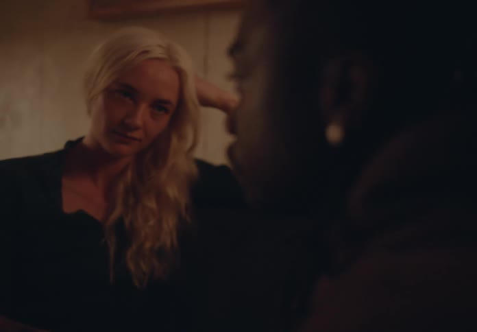 In a dimly lit room a woman with blonde hair looks at a person with dark hair from across a table