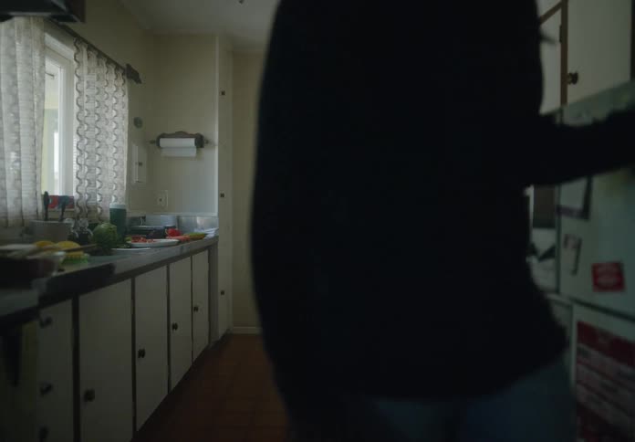 A young couple in a kitchen at home shows obvious distress likely after a fight the man leaves the kitchen while the woman stands against a door crying