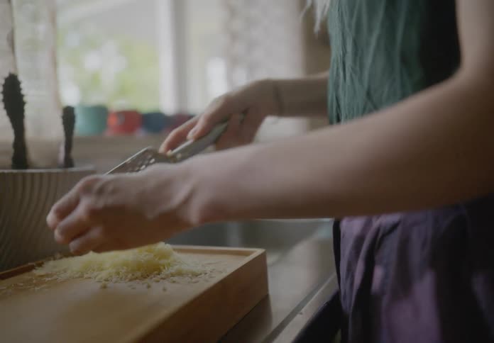 Woman grating cheese on wood block near kitchen window
