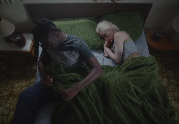Man lying in bed next to a woman gets up