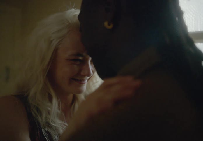 A couple hug and flirt playfully in a dimly lit room near a window