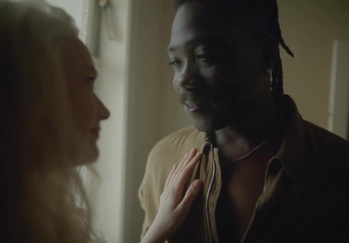 A couple hugs and flirts playfully in a dimly lit room near a window