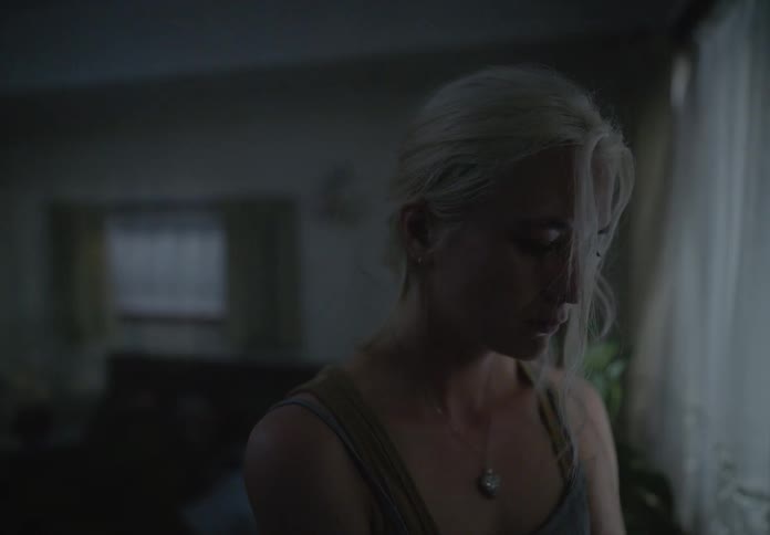 Woman standing in a dimly lit room with a sad facial expression
