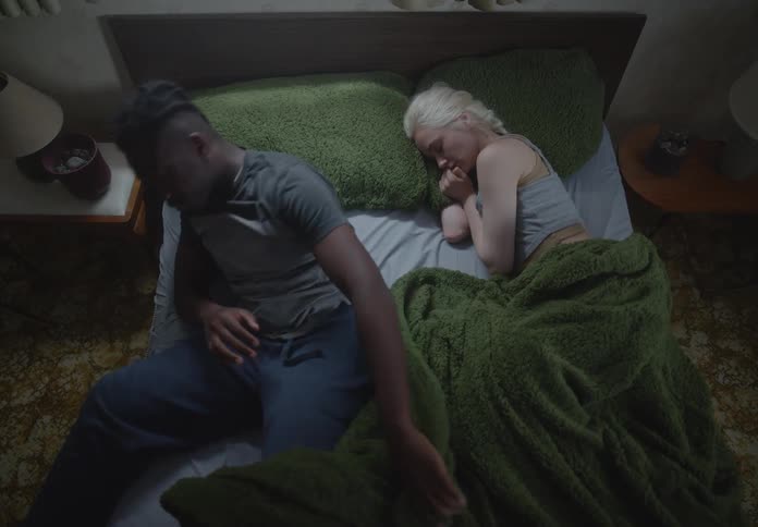 A couple in bed the man restlessly stands up leaving the woman alone