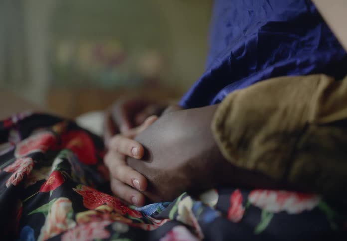 Two pairs of hands one dark skinned and one light skinned rest gently on a patterned fabric with a blue garment partially visible
