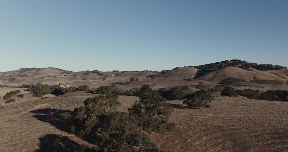 Rural homes dot hilly terrain under a blue sky