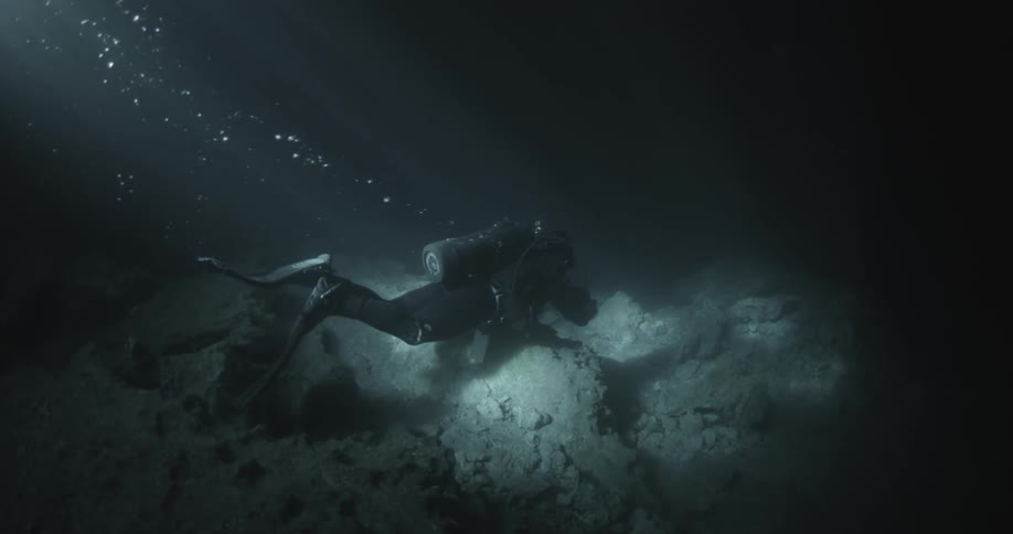 A diver swims to the bottom of the ocean and flashes a light
