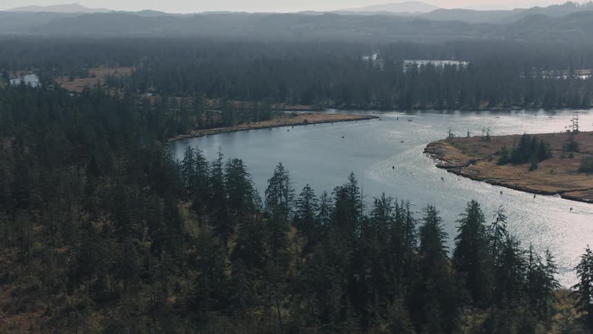 River winds past fields and forests near the mountains on a foggy day