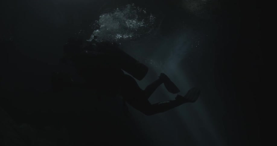 A scuba diver underwater swimming around in slow motion and making bubbles