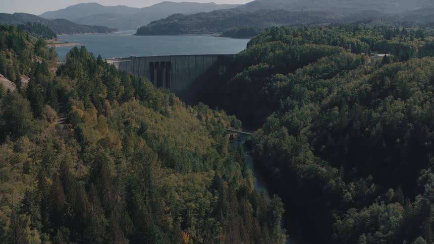 Aerial view of a huge dam surrounded by mountains and forests