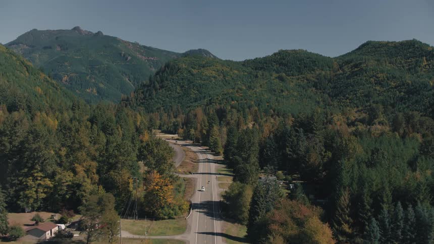 Aerial shot of a highway surrounded by mountains and forests