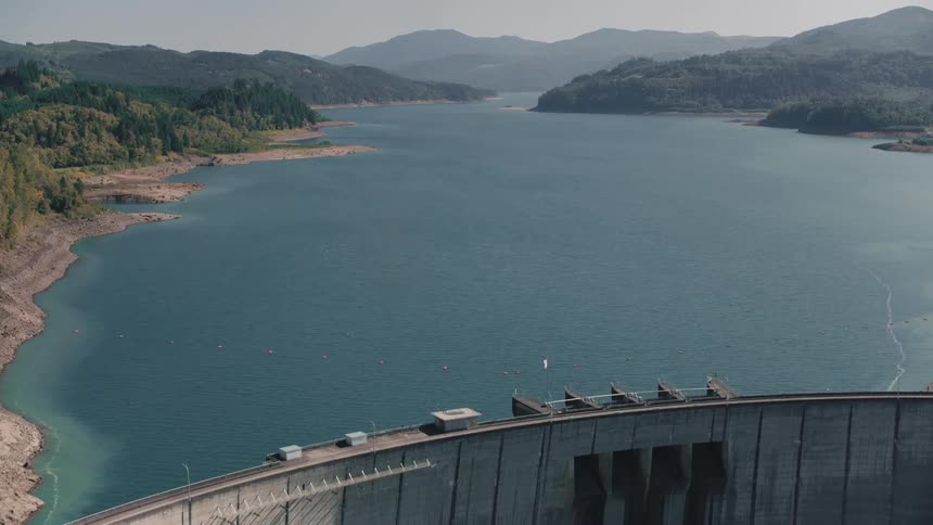 Aerial view of a dam over a wide river surrounded by mountains