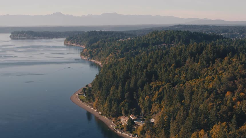 Aerial panorama of a bay with forest surrounded by the sea and mountains on the horizon