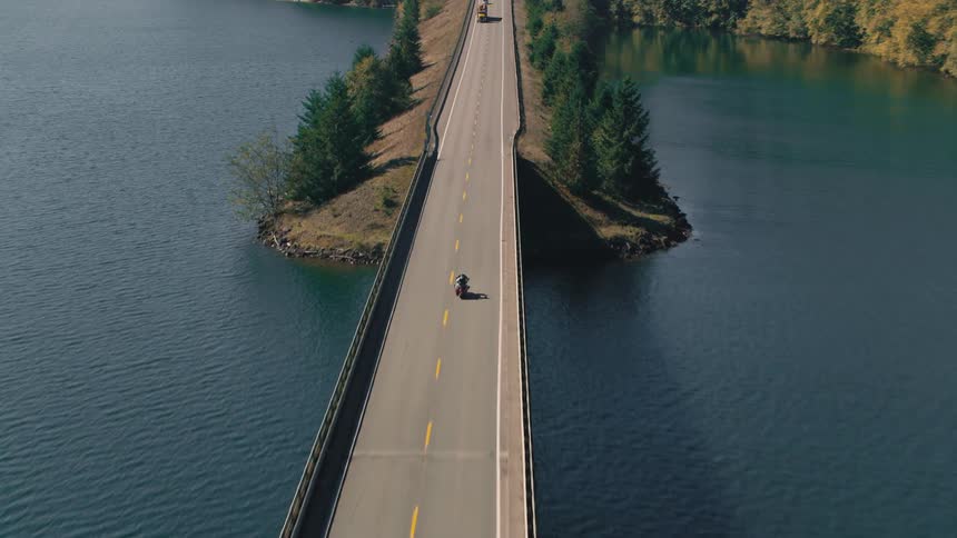 Aerial view of a person on a motorcycle traveling along a highway crossing a river