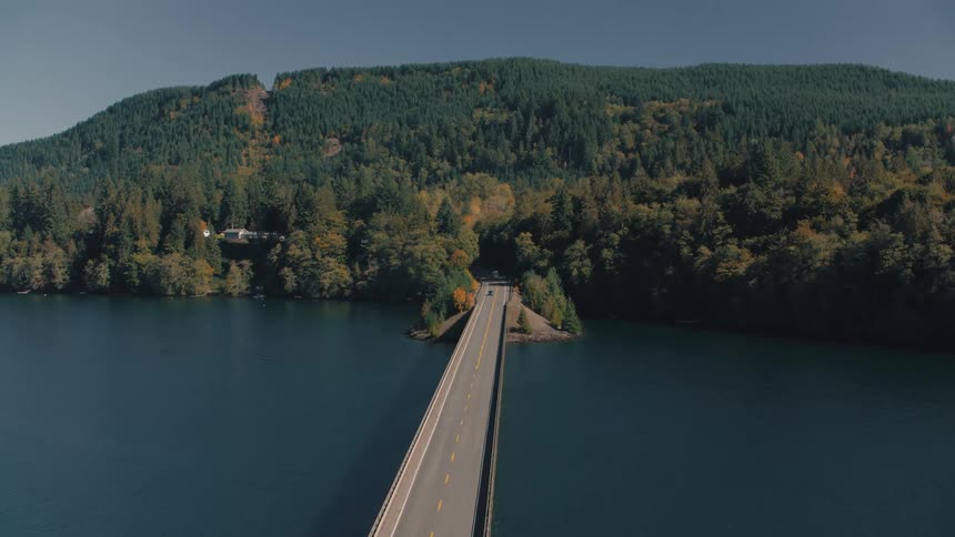 Aerial view of a long highway that crosses a river and leads to a mountain access with dense forest