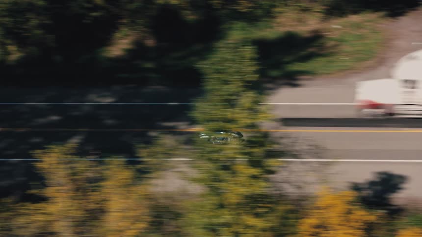 A motorcyclist riding a cruiser style motorcycle on an open highway surrounded by fields and trees under a clear sky