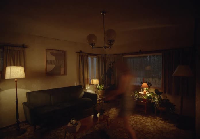 A young couple cuddles in a living room surrounded by plants and lamps providing warm lighting