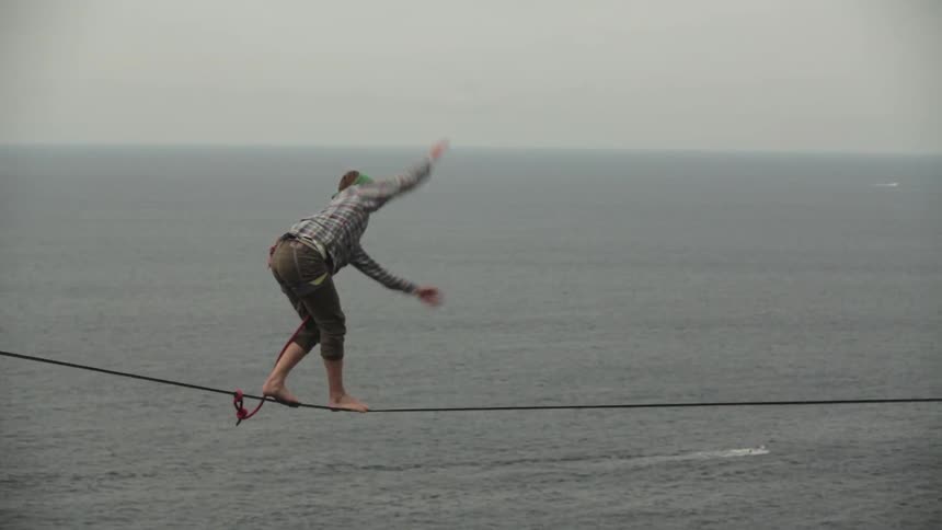 Person walking a high wire next to a large body of water falling and catching themselves