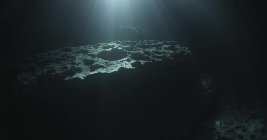 Light shines on some rocks in the dark waters below