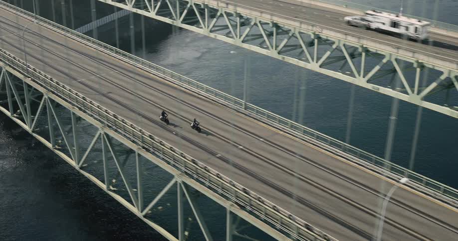 Aerial of two people riding motorcycles across a steel bridge on an early autumn day