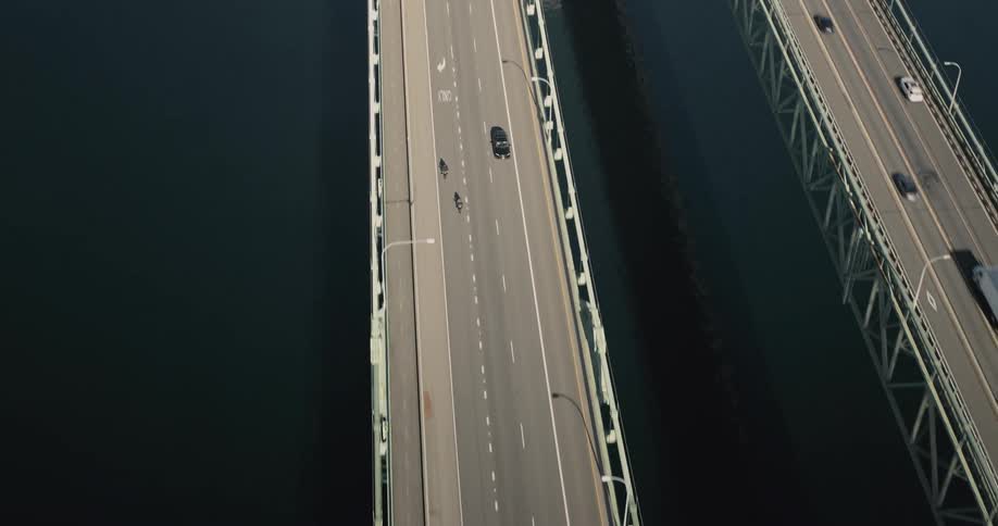 Motorcyclists cross a busy bridge over dark blue water during the daytime