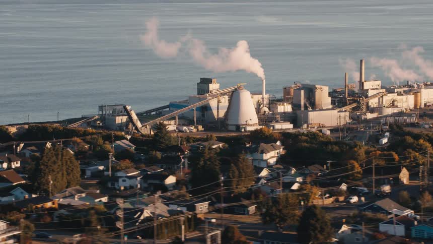 Aerial view of a factory exhaling pollutants on the seashore and an urban city in the foreground