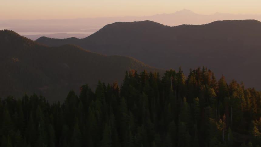 An aerial view reveals a treecovered mountain peak with layers of hills extending into the hazy distance