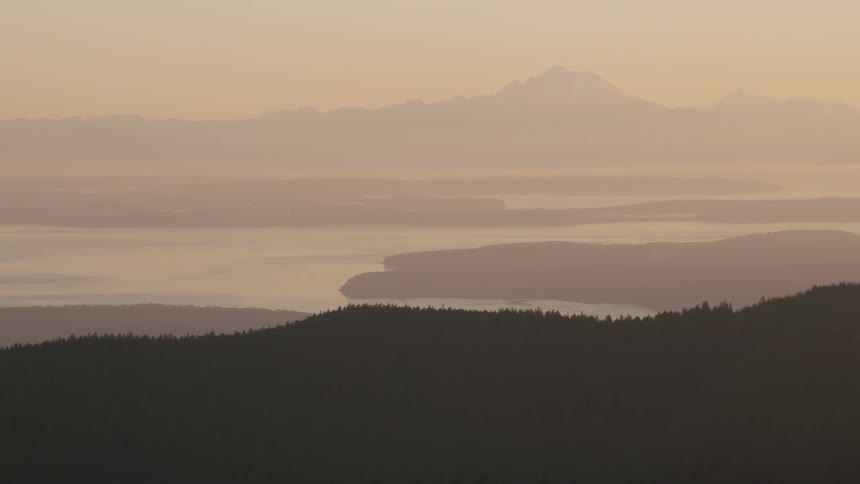 A hazy layered landscape shows silhouetted hills distant islands and a mountain peak in the background